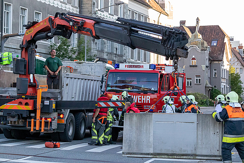 Mitglieder der Feuerwehr und die Firma Bickel beim Anbringen der Betonelemente auf der Illbrücke mithilfe eines Krans.