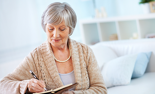 Eine ältere Frau schreibt in ein kleines Buch.