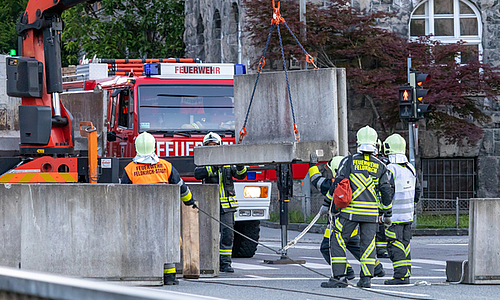 Mitglieder der Feuerwehr und die Firma Bickel beim Aufstellen der Betonelemente auf der Illbrücke mithilfe eines Krans. 