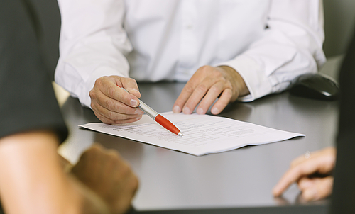 Ein Mann zeigt mit einem Stift auf ein Formular, das auf dem Tisch liegt. 