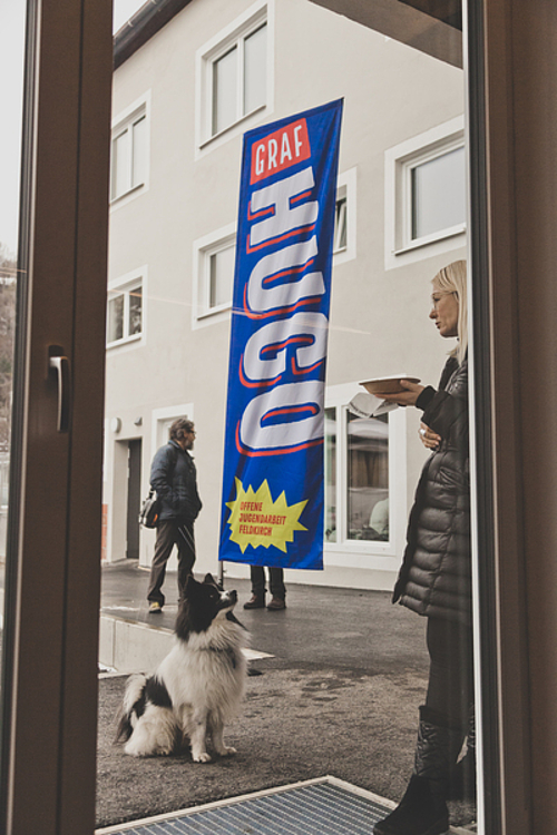 Fahne Graf Hugo hinter verschlossener Glastüre, ein Hund und eine Frau