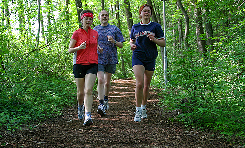Zwei Frauen und ein Mann joggen auf der Naturlaufbahn.