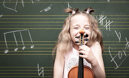 Ein kleines Mädchen steht vor einer Tafel und hält eine Geige in der Hand.