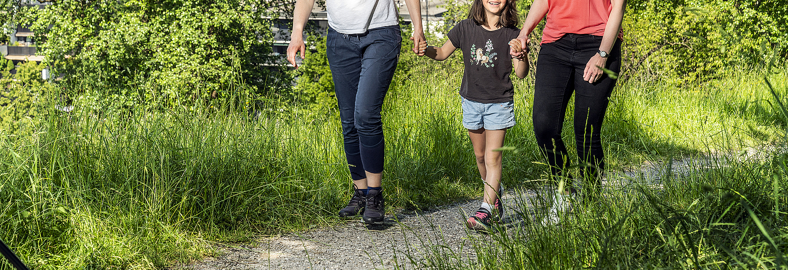 Zwei Frauen und ein Mädchen spazieren auf einem Weg in der Natur.