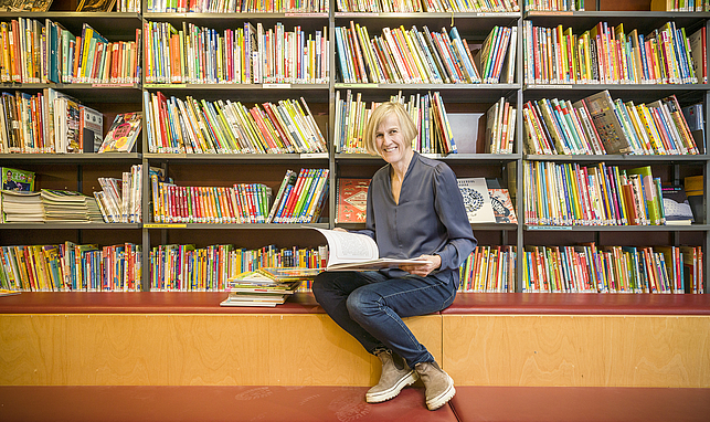 Eine Frau sitzt vor einem Bücherregal und hält ein offenes Buch in den Händen