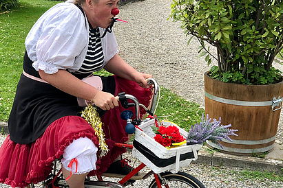 Eine Frau mit einer Clownsnase fährt auf einem kleinen Fahrrad.
