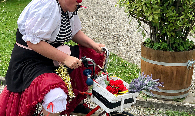 Eine Frau mit einer Clownsnase fährt auf einem kleinen Fahrrad.