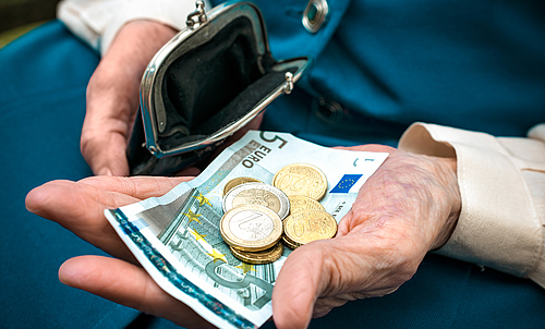 Eine ältere Person hält in der einen Hand ein paar Münzen und einen 5-Euro-Schein und in der anderen Hand eine kleine Geldtasche.