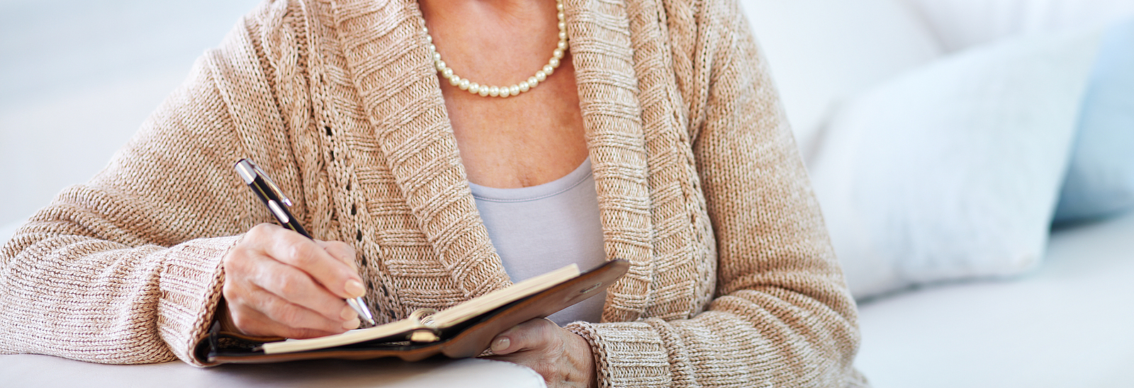 Eine ältere Frau schreibt in ein kleines Buch.