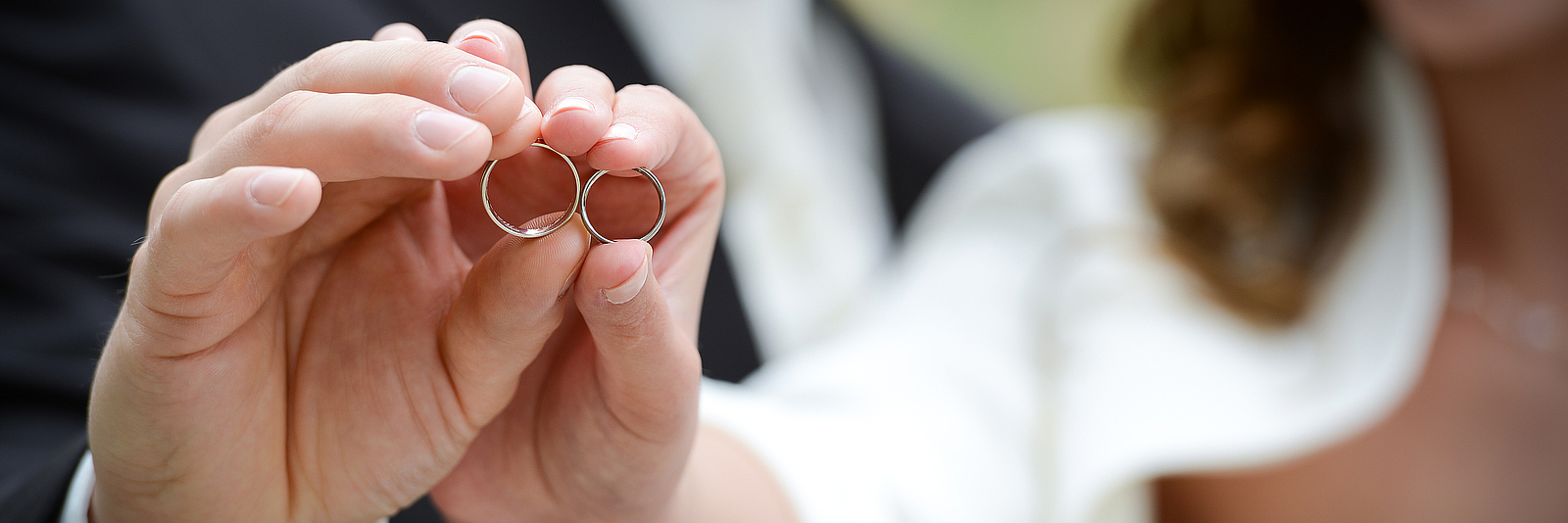 Ein Mann und eine Frau halten je einen Ehering in einer Hand. 