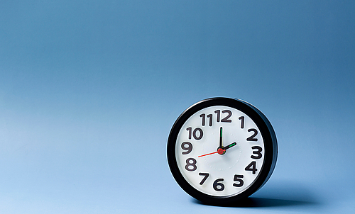 Black alarm clock isolated on blue background. The clock set at 2 o'clock.