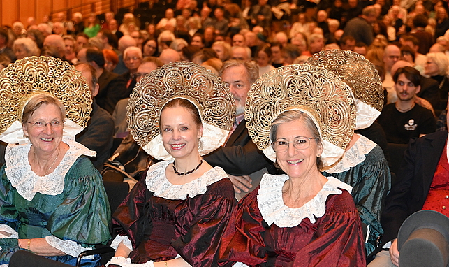 Drei Frauen sitzen in Tracht im Publikum.