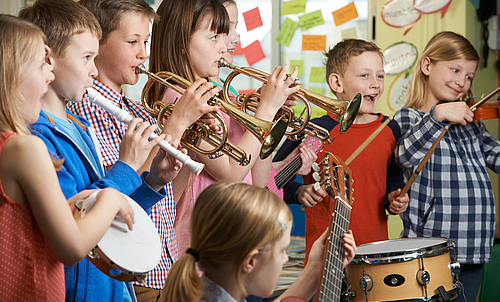 Mehrere Kinder stehen nebeneinander und spielen verschiedene Instrumente. 