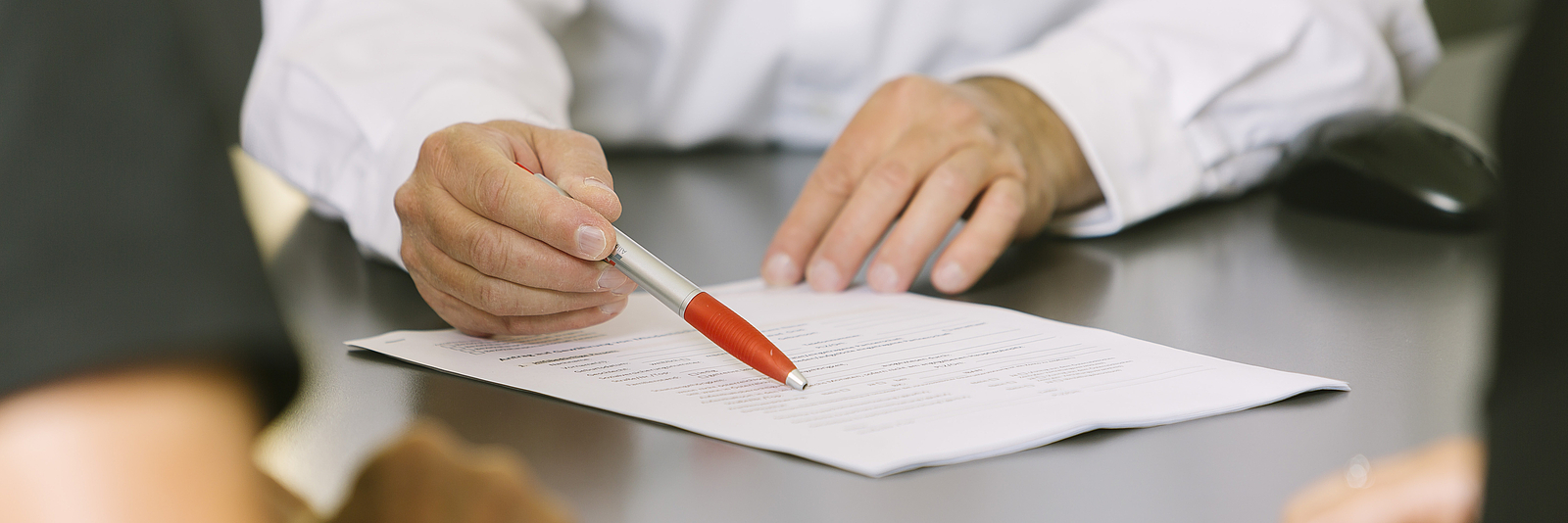 Ein Mann zeigt mit einem Stift auf ein Formular, das auf dem Tisch liegt. 
