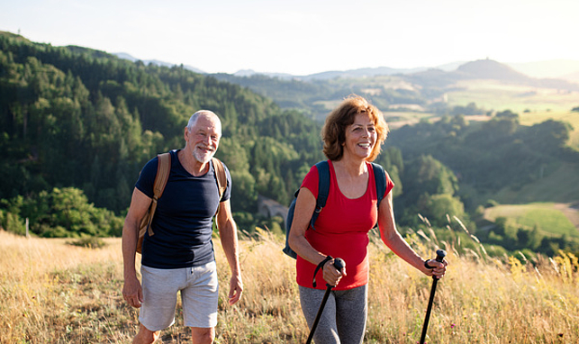 Ein älterer Herr und eine ältere Frau wandern durch die Natur.