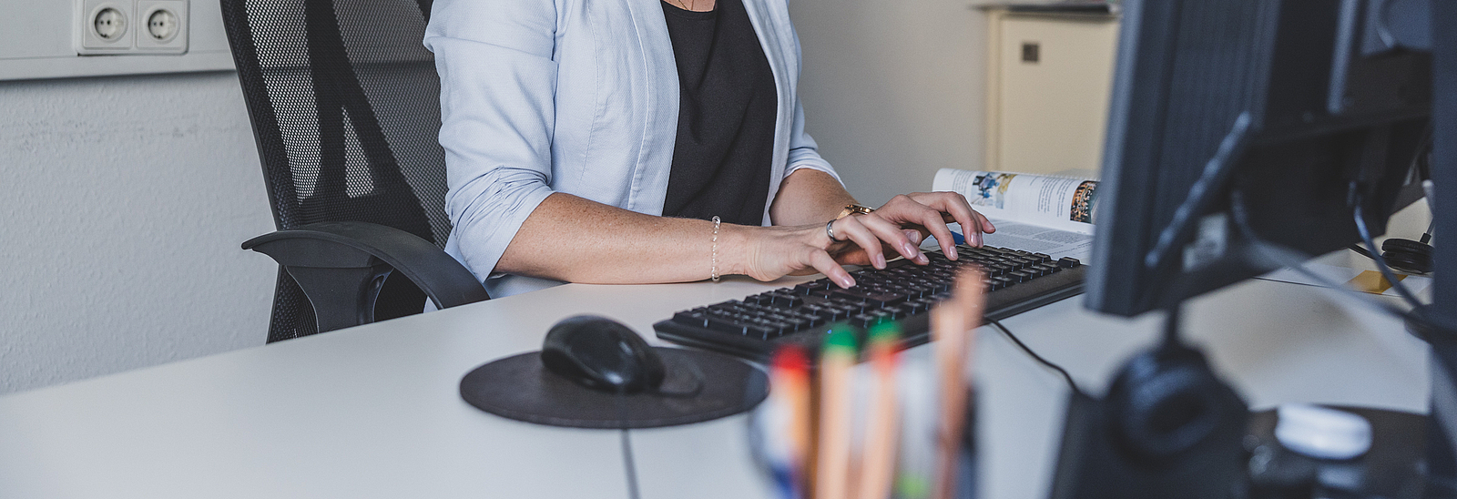 Eine Frau sitzt vor einem Computer und tippt auf eine Tastatur.