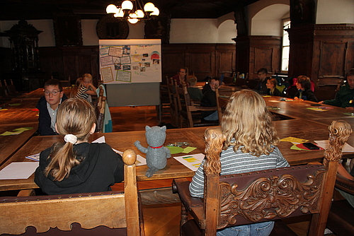 Die Kinder sitzen im Ratssaal, in der Mitte steht ein Flipchart.