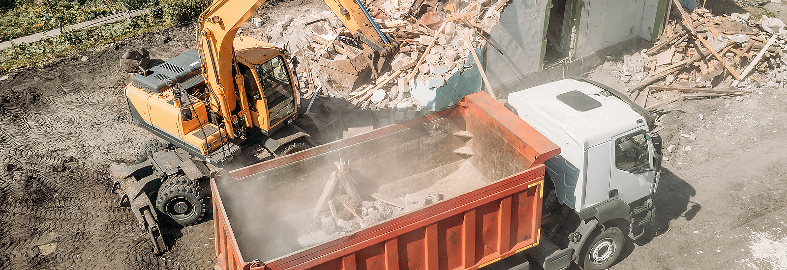 Excavator loads construction debris of old building after destruction in dump truck, aerial view