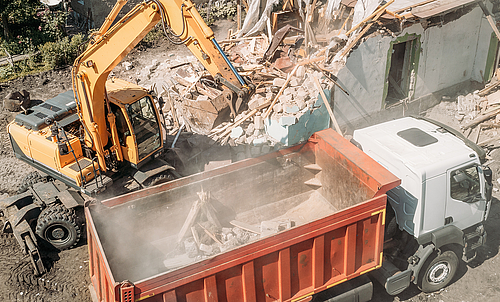Excavator loads construction debris of old building after destruction in dump truck, aerial view