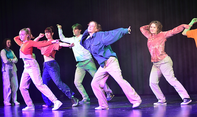 Eine Gruppe Jugendlicher steht auf einer Bühne und tanzt.